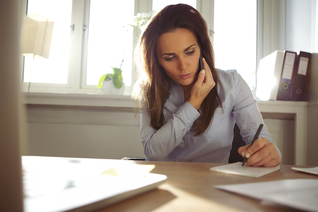 Young female writing notes while talking on phone