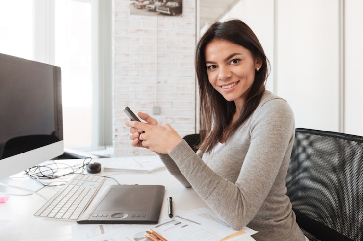 Cheerful businesswoman using computer and phone